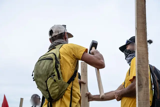 Dos personas con camiseta amarilla clavan una estaca a mazazos en el campo