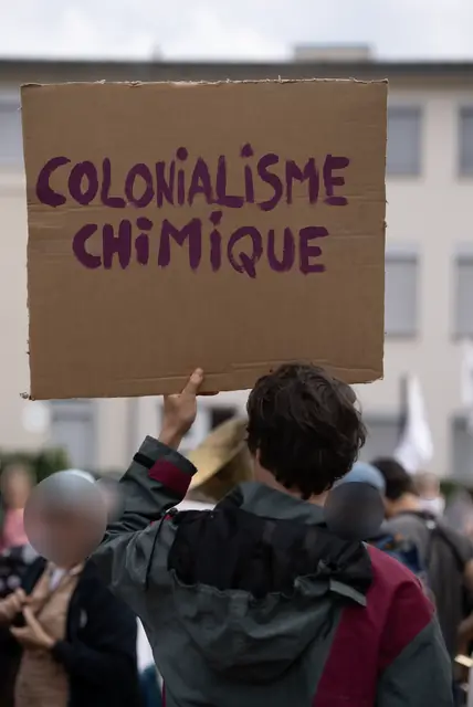 Una pancarta de cartón «Colonialismo químico» («Colonialisme chimique») alzada sobre la multitud