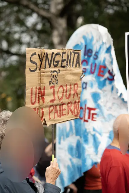 متظاهرة ترفع لافتة «سينجنتا، يومًا ما ستدفعين الثمن» («Syngenta, un jour tu paieras»)